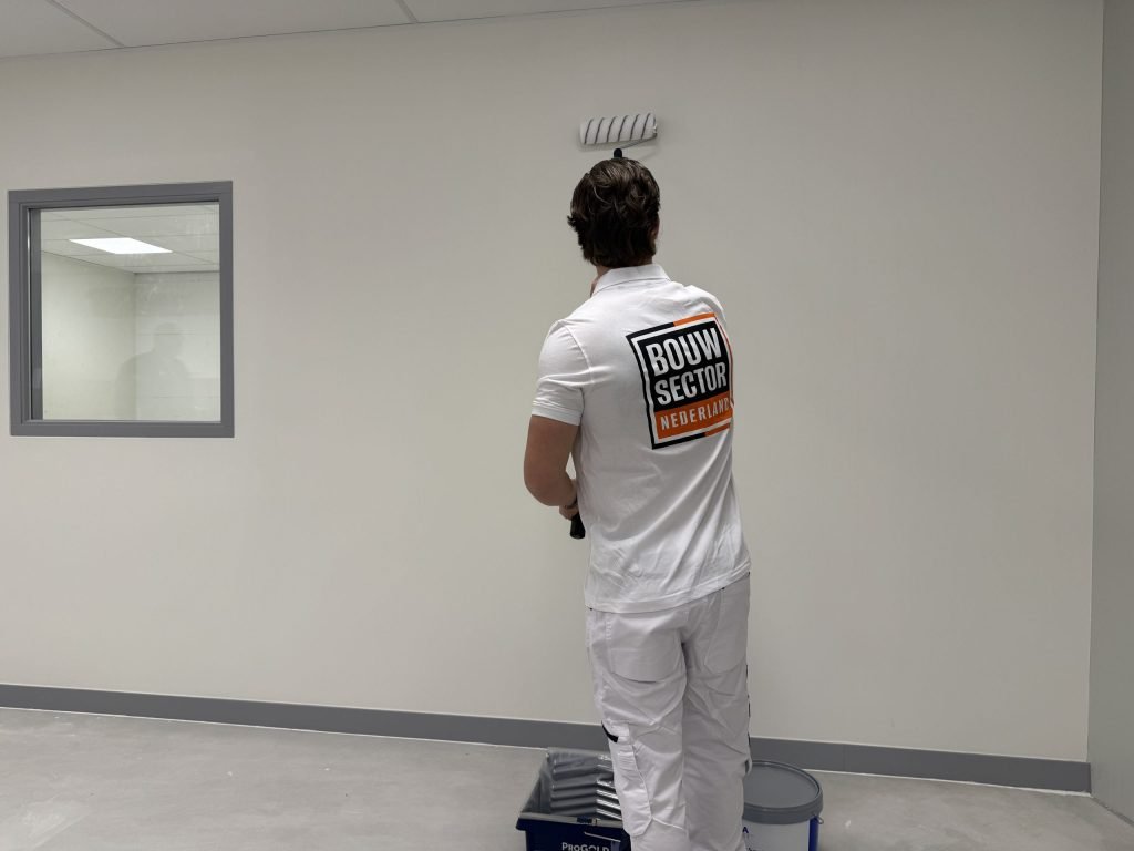 Schilder van Bouwsector Nederland rolt een lichte muur in een lege ruimte met een binnenraam