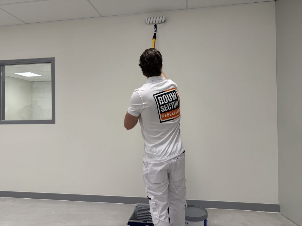 Schilder werkt de bovenkant van een muur bij het plafond af met een roller op verlengsteel