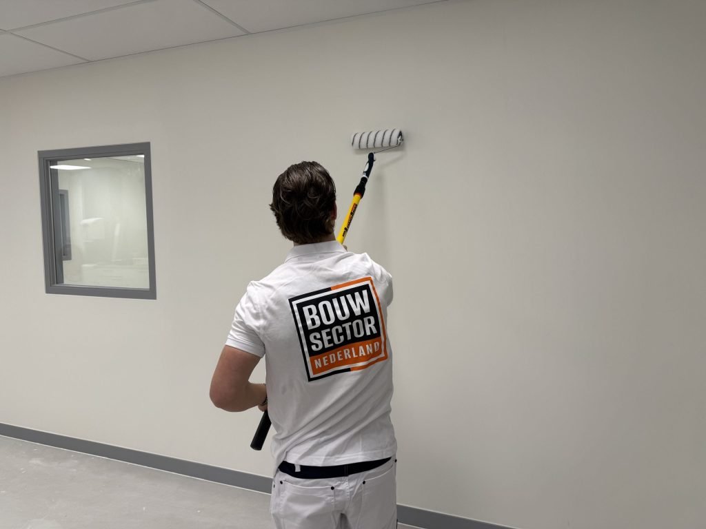 Schilder in witte werkkleding zet een lichte wand met de roller in de verf