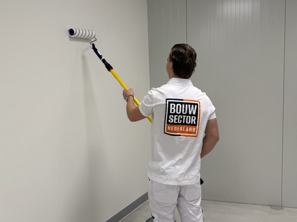 Vakman van Bouwsector Nederland saust een witte muur met een roller aan een steel