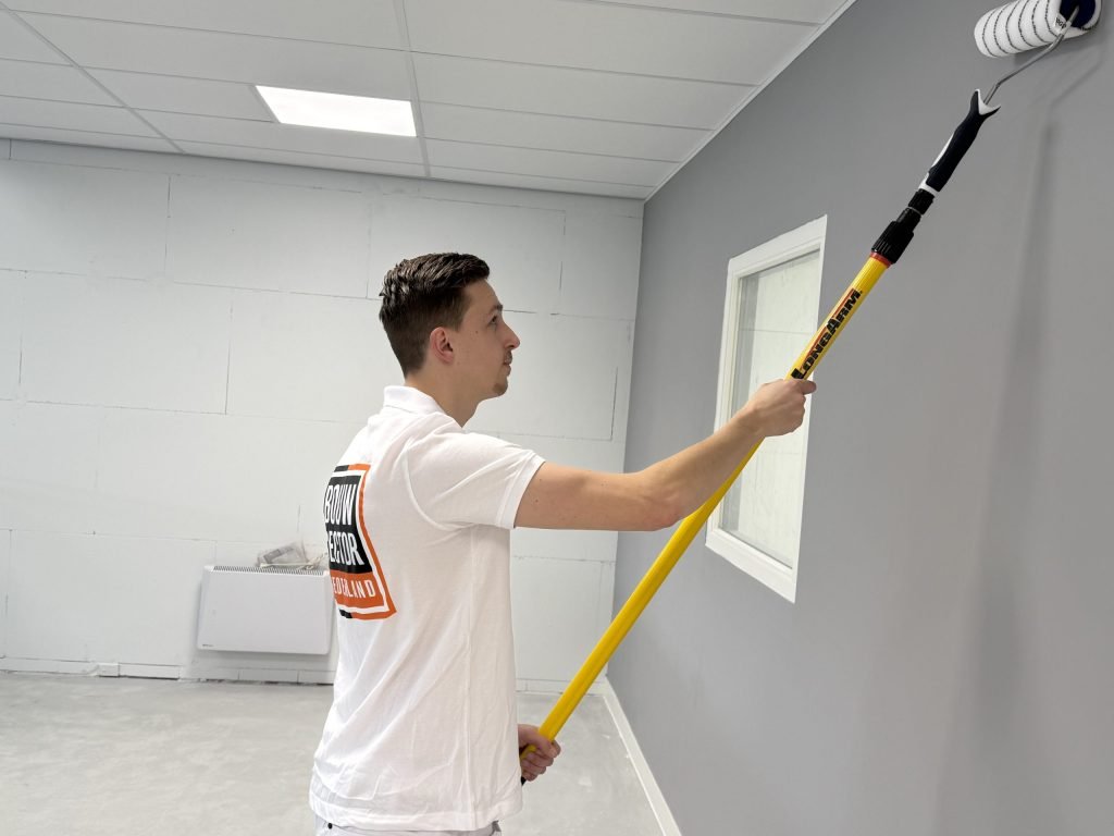 Schilder met het logo van Bouwsector Nederland rolt een grijze muur naast een raam