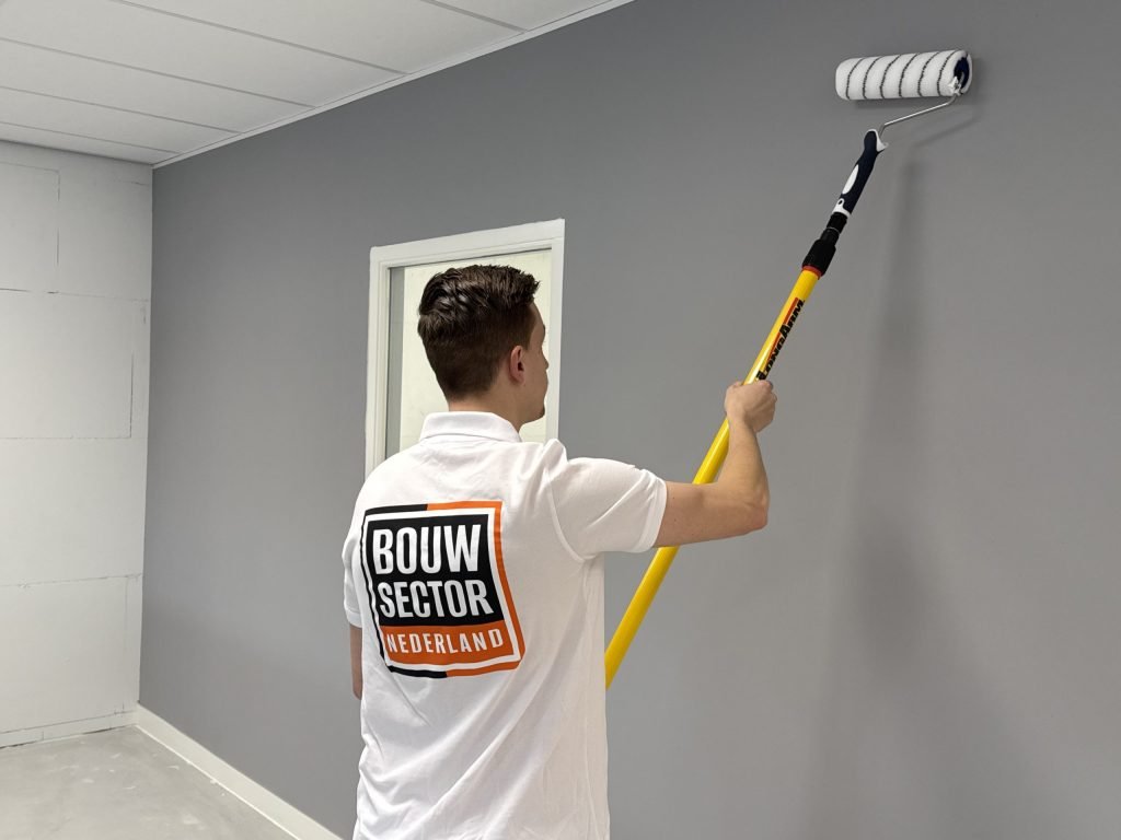 Schilder rolt een grijze muurverf op de wand van een kamer met een witte deur