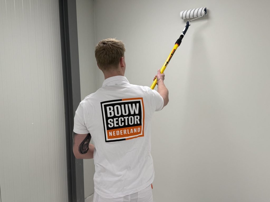 Schilder van Bouwsector Nederland brengt met een lange roller verf aan op een wand in een gang