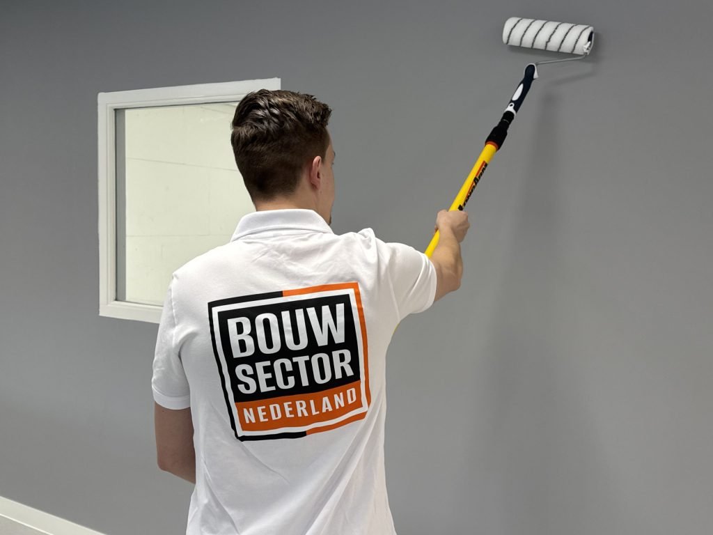 Schilder van Bouwsector Nederland, op de rug gezien, rolt een grijze muur naast een raam met witte omlijsting
