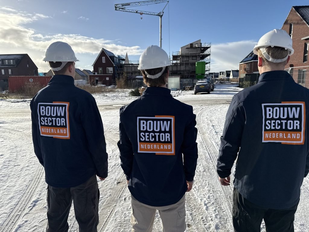 Drie vakmensen van Bouwsector Nederland met helm, gezien op de rug, bij nieuwbouwwoningen in de sneeuw